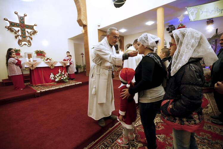 A priest gives Communion during Christmas Eve Mass at Sacred Heart Catholic Church in Baghdad. (CNS photo/ Thaier Al-Sudani, Reuters)