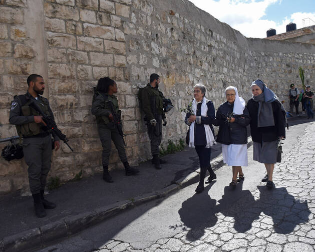 Women religious carry olive branches past Israeli border police before the annual Palm Sunday procession on the Mount of Olives overlooking the Old City of Jerusalem on March 20. (CNS photo/Debbie Hill)