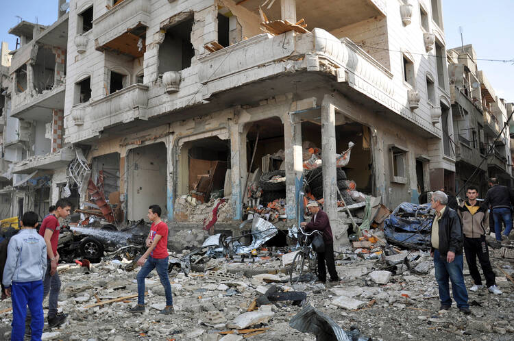 People walk in front of destroyed buildings in late February at the site of a twin bomb attack in the city of Homs, Syria. (CNS photo/EPA)