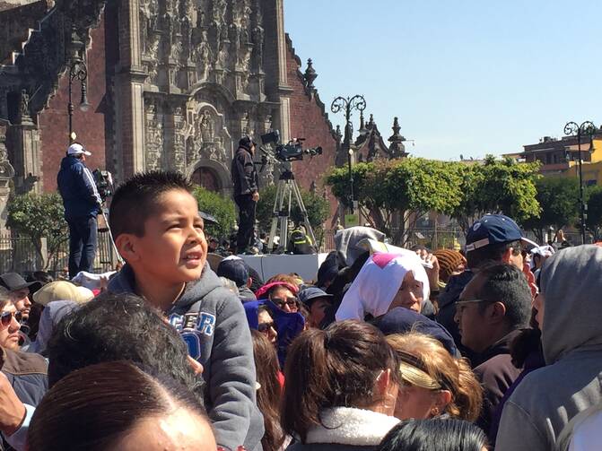 Watching Francis. A young boy with the crowd in Mexico City's historic Zocalo watches Pope Francis on a jumbo screen as he speaks to Mexico's bishops on Feb. 13. (Photo by Kevin Clarke)