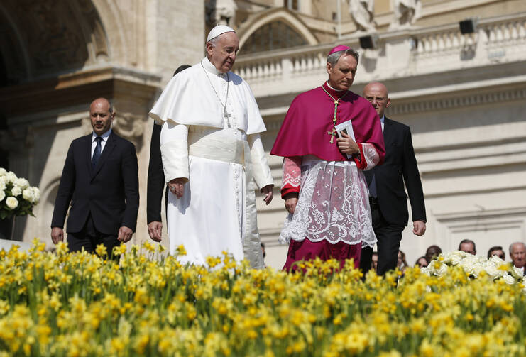 Pope Francis walks past flowers as he prepares to greet the crowd at the conclusion of Easter Mass in St. Peter's Square at the Vatican March 27. Also pictured is Archbishop Georg Ganswein, prefect of the papal household (CNS photo/Paul Haring).