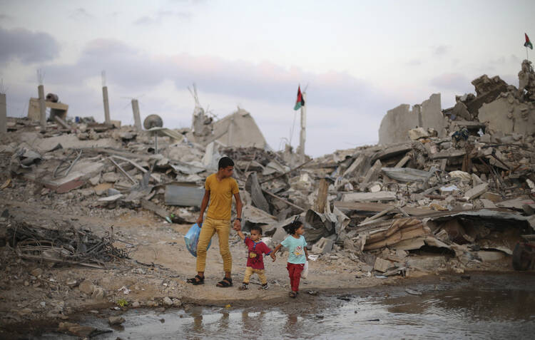 Palestinians in Gaza walk next to the ruins of houses destroyed during the Israeli offensive. (CNS photo/Ibraheem Abu Mustafa, Reuters)