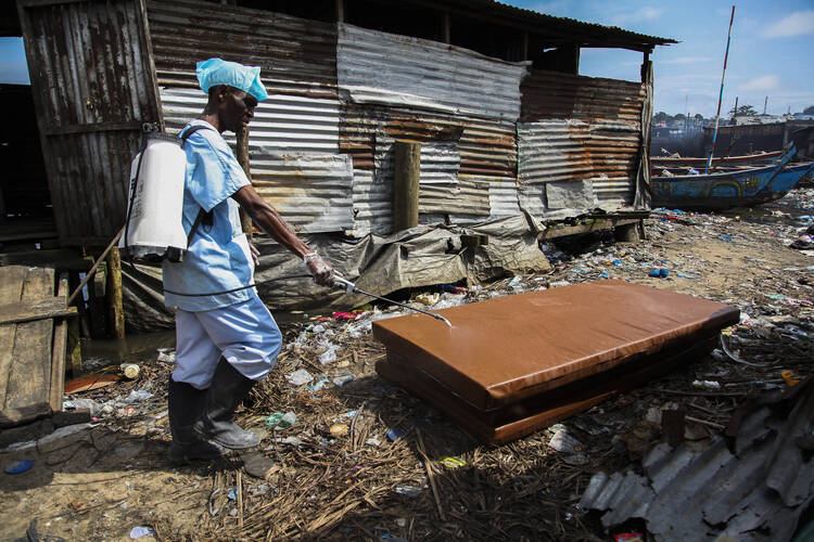 A Liberian nurse disinfects a looted mattress taken from a school that was used as an Ebola isolation unit in Monrovia, Liberia, on Aug. 19. (CNS photo/Ahmed Jallanzo, EPA)
