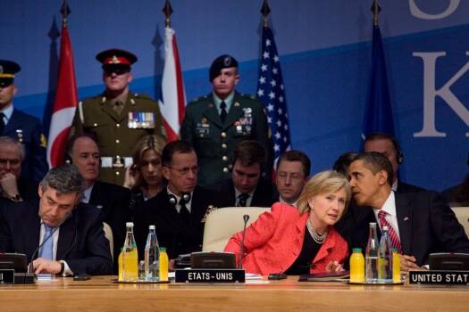 President Obama and Hillary Clinton speaking with one another at the 21st NATO summit, April 2009 (Photo via Wikimedia Commons)