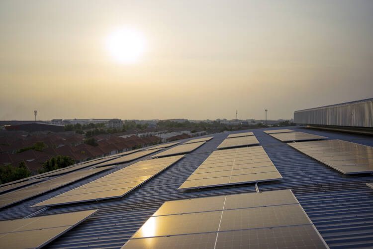The sun rises above an array of rooftop solar panels,