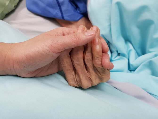 A picture of a person holding an older person's hand who is in the hospital