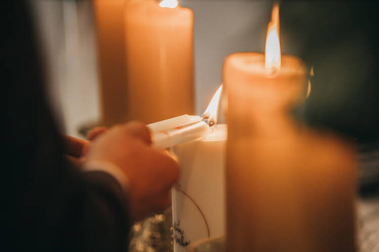 A closeup of a couple's hands as they light church candles (iStock/Wirestock)