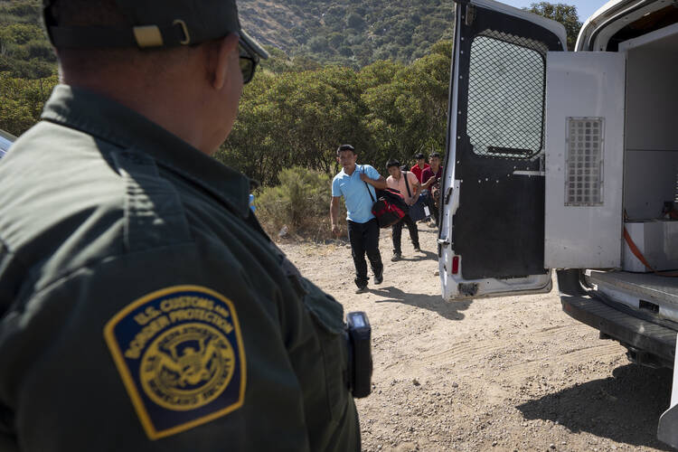 A Border Patrol agent leads a group of migrants seeking asylum toward a van to be transported and processed on June 5, 2024, near Dulzura, Calif. (AP Photo/Gregory Bull)