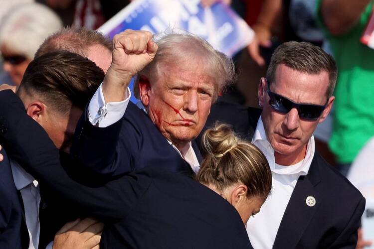 Republican presidential candidate and former U.S. President Donald Trump gestures, with blood on his face, is assisted by guards after shots were fired during a campaign rally at the Butler Farm Show in Butler, Pa.