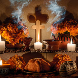 small altar with orange flowers around with cross and smoke in the middle, some dia de los muertos items on the altar in front of the cross